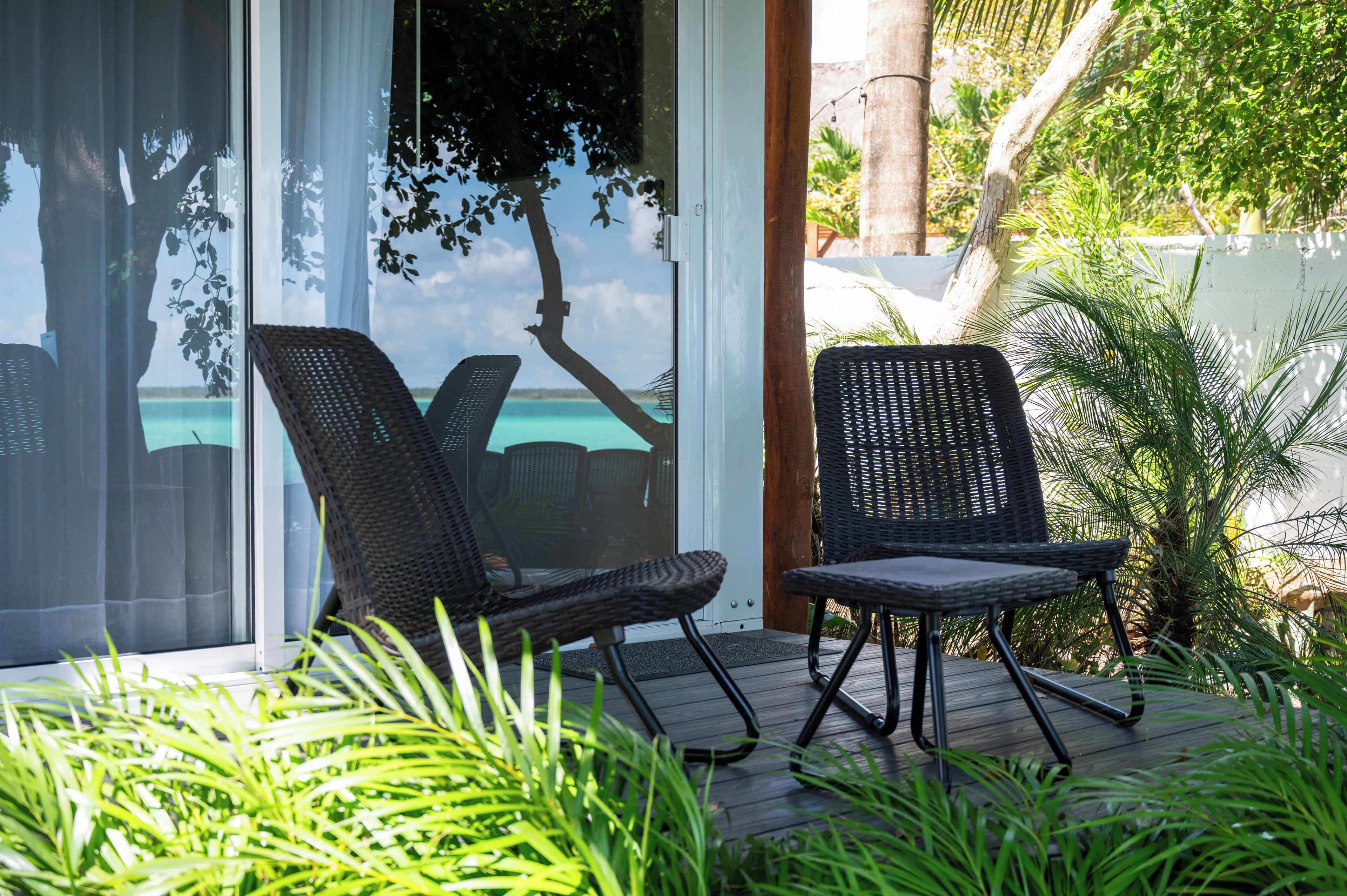 A patio with two wicker chairs, a wooden deck, and a view of the ocean through a glass door.