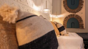 Una cama con colchón blanco, almohada gris oscuro y almohada a rayas. Hay dos lámparas fijadas a la pared y dos obras de arte mural con diseños circulares.