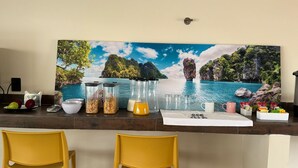 Una encimera de cocina con un cuadro de paisaje, dos sillas amarillas y diversos utensilios de cocina.