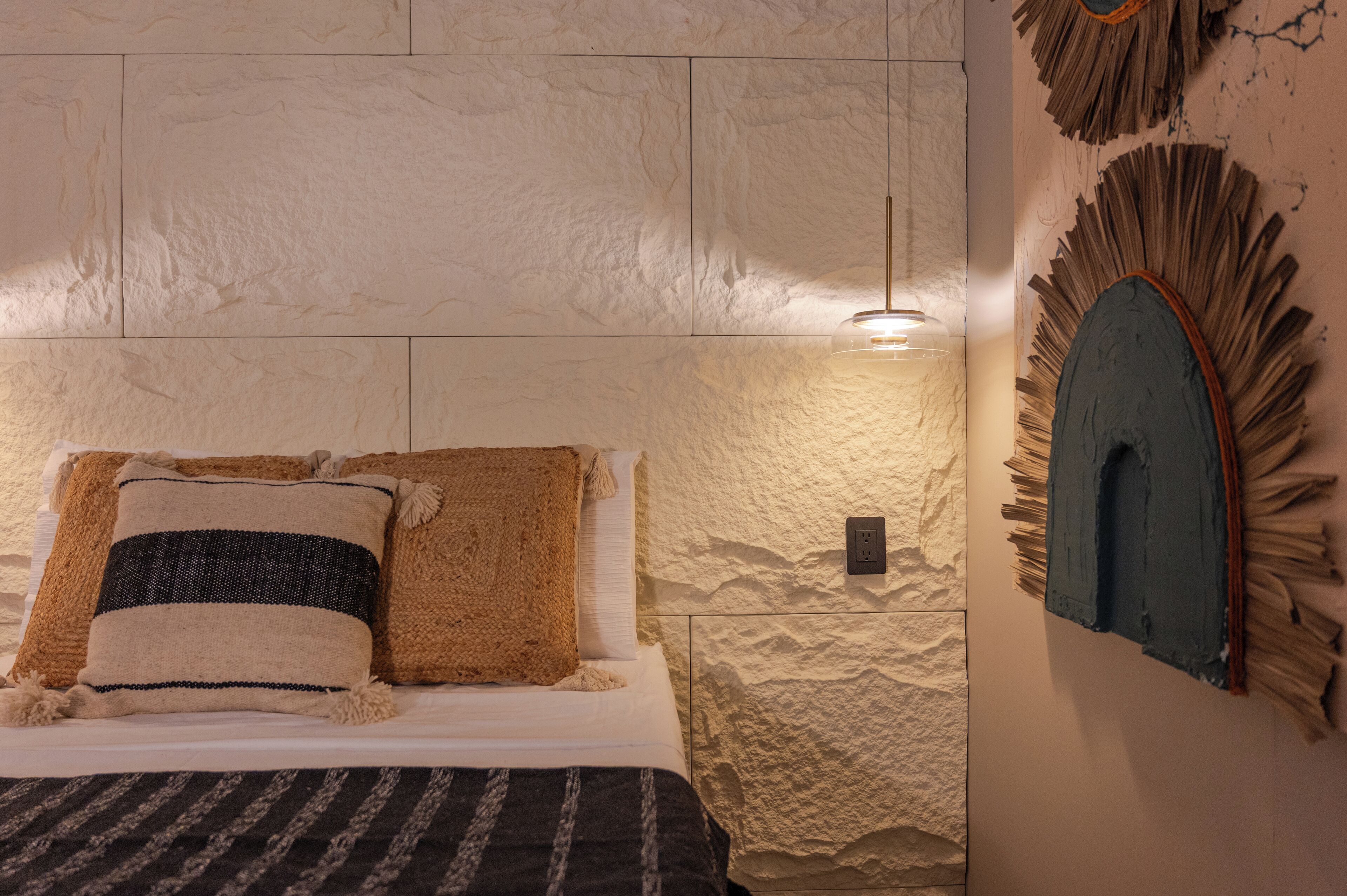 Quarto com parede texturizada, cama com roupa de cama listrada e luminária fixada na parede.