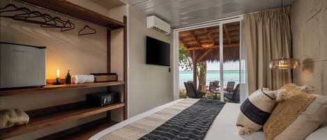 A bedroom with a bed, bedside tables, a TV, and a view of the ocean.
