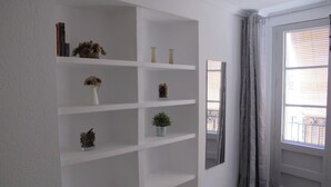 Une pièce avec un mur blanc, une grande fenêtre avec des stores et une porte avec un rideau.