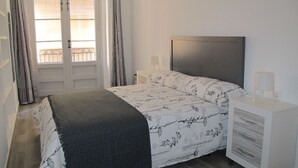 Une chambre à coucher comprenant un lit, une table de chevet, une commode, une fenêtre avec des rideaux et une porte.