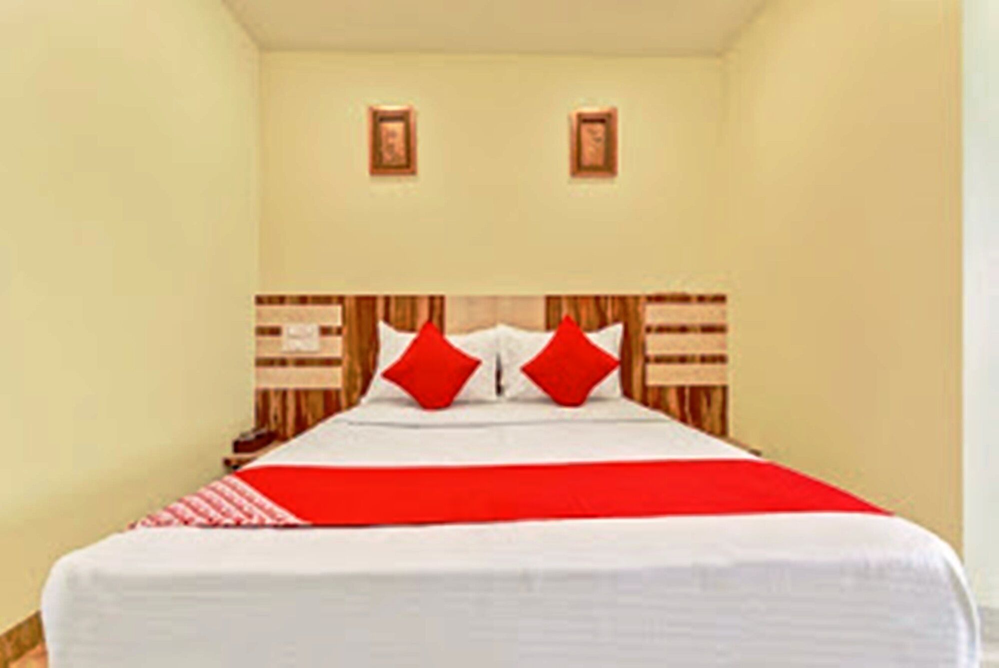 A hotel room with a large bed, two red pillows, and a red and white bedspread.