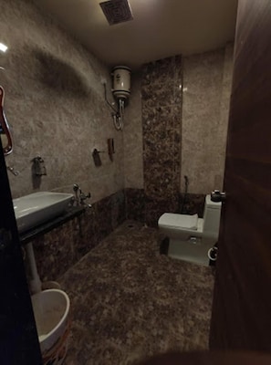 A bathroom with a marble floor, a sink, a toilet, and a shower area. - Hotel Manik (Chhatrapati Sambhajinagar)