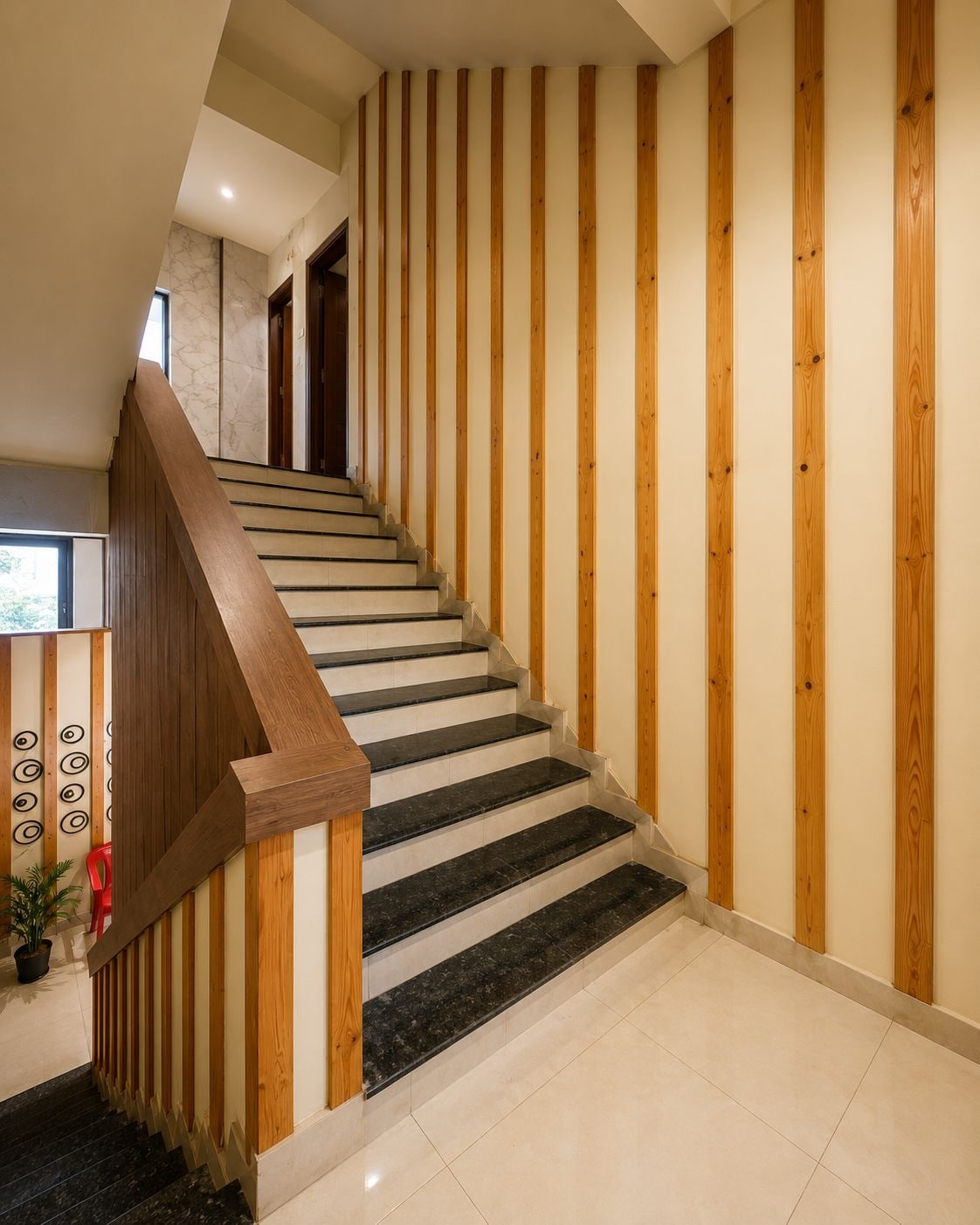 A modern staircase with wooden handrails and black steps, leading to a landing with a potted plant and a red chair.