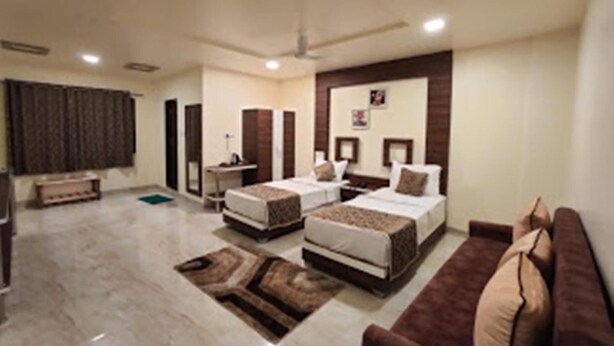 A hotel room with two beds, a sofa, a desk, and a large window. - Hotel Manik (Chhatrapati Sambhajinagar)