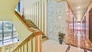 A modern interior with a wooden staircase, a stone wall, and a tiled floor. - Hotel Manik (Chhatrapati Sambhajinagar)