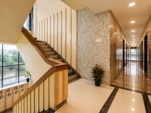 Un interior moderno con una escalera de madera, paredes de mármol y un pasillo que conduce a un ventanal con vistas.