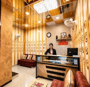 A reception area with a receptionist, a clock, a check-out time sign, a reception desk, and a sofa. - Hotel Manik (Chhatrapati Sambhajinagar)