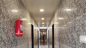 A marble-floored hallway with a fire extinguisher on the left wall and a sign on the right wall. - Hotel Manik (Chhatrapati Sambhajinagar)