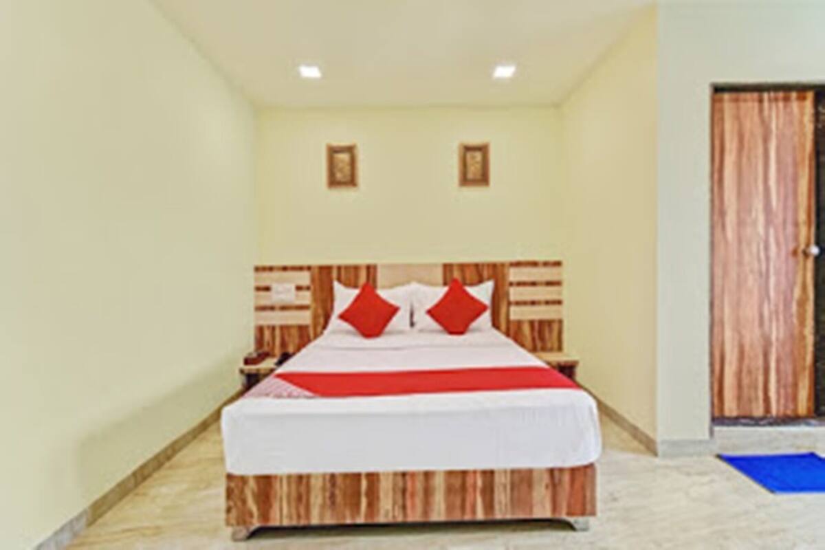 A hotel room with a wooden headboard, a bed with white bedding and red pillows, a nightstand, and a door with a wooden panel.