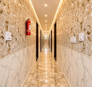A corridor with marble flooring, wall-mounted fire extinguishers, and light switches. - Hotel Manik (Chhatrapati Sambhajinagar)