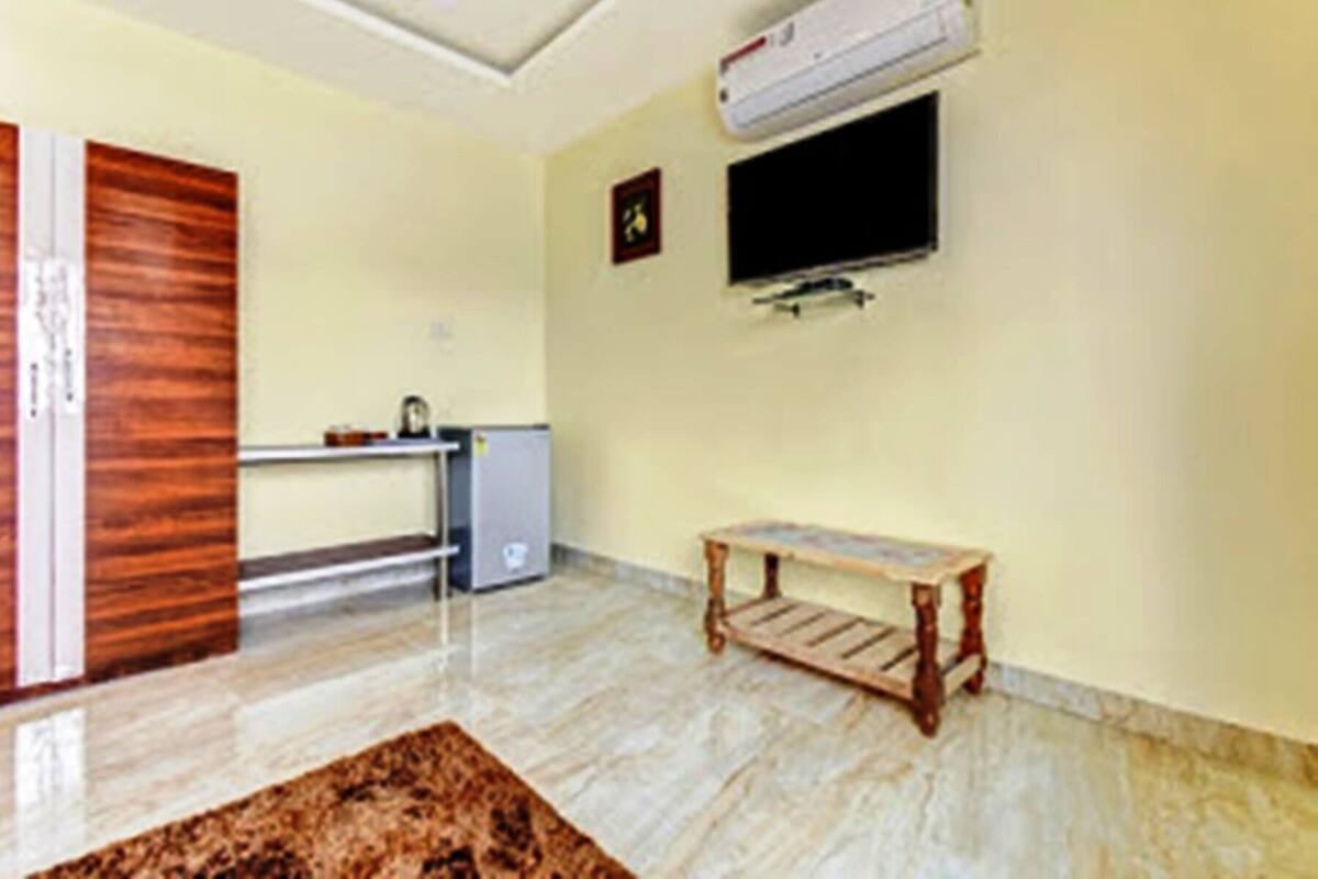 A room with a wooden door, a small desk with a chair, a television mounted on the wall, and a marble floor.