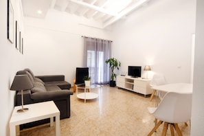 A modern living room with a sofa, a coffee table, a TV, and a dining area. - Central 3-Bedroom Apartment (Alicante (Alacant))