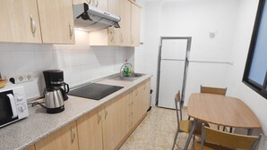 Eine kompakte Küche mit Holzausstattung, einer Mikrowelle, einer Kaffeemaschine und einem Spülbecken. Ein kleiner Esstisch mit zwei Stühlen steht daneben.
