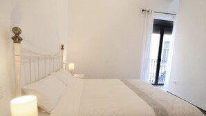 Ein Schlafzimmer mit Bett, weißer Bettwäsche, einer Nachttischlampe und Blick auf einen Balkon.