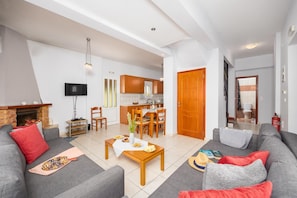 A modern living room with a fireplace, grey sofas, a wooden coffee table, and a dining area with wooden chairs.