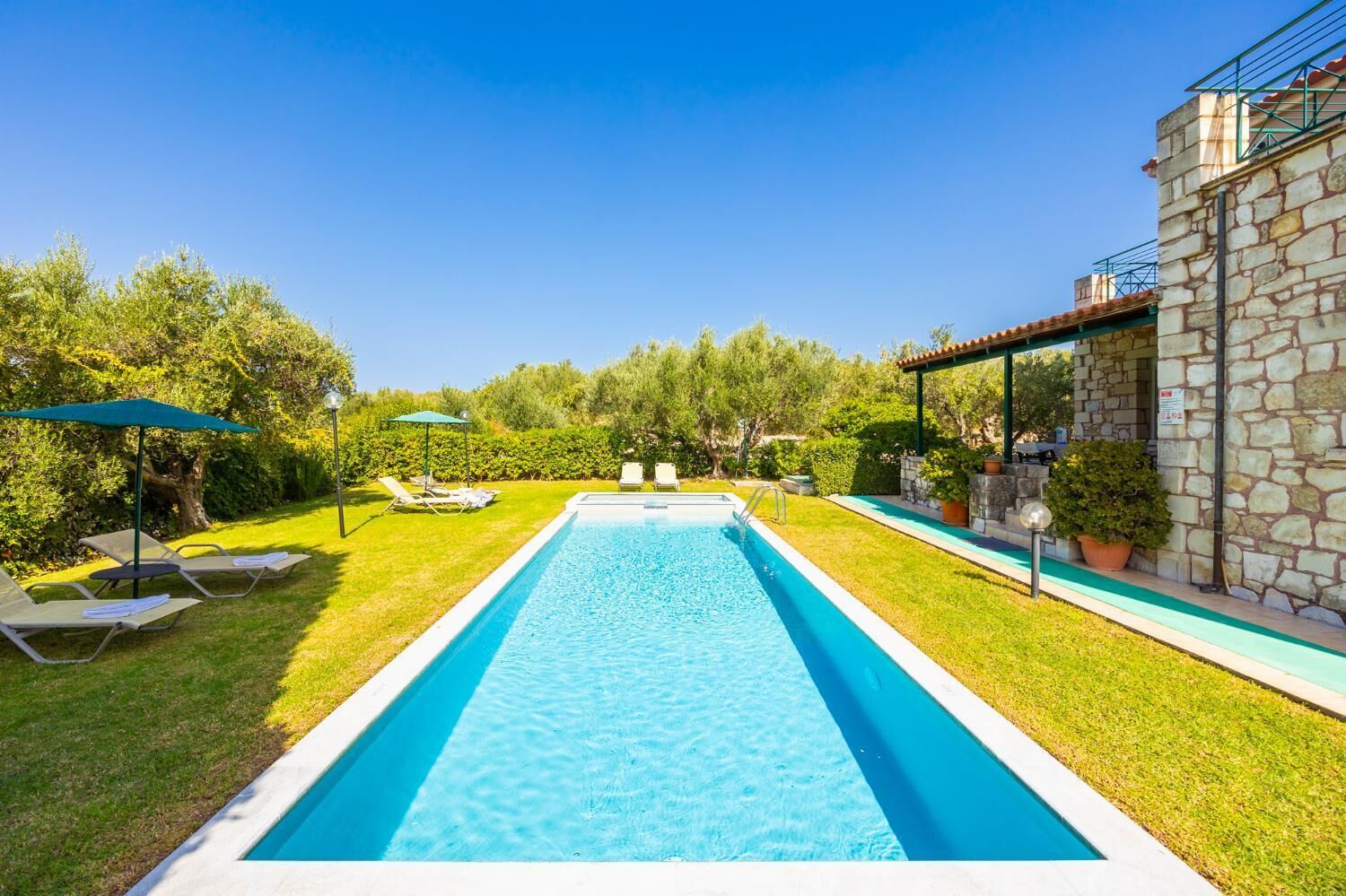 Ein rechteckiger Pool mit einer Steinmauer an einer Seite und einer überdachten Terrasse auf der anderen.