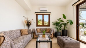 Ein Wohnzimmer mit gemusterten Sofas, einem Couchtisch und großen Kübelpflanzen.
