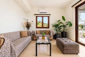 Una sala de estar con sofás estampados, una mesa de centro y plantas grandes en macetas.