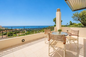 Un balcon avec une table et des chaises, une plante en pot et une vue sur la mer.