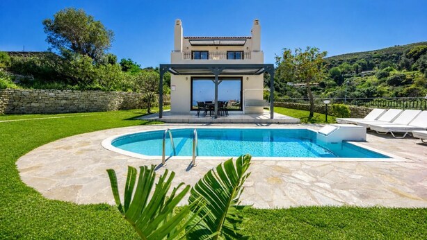 Eine moderne Villa mit Pool, Sitzgelegenheiten im Freien und einer Steinmauer.
