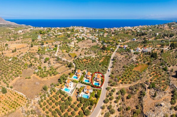 An aerial view of a coastal residential area with houses, a road, and a swimming pool complex. - Ekklisies Tria Large Private Pool, A/C, WiFi (Apokoronos)