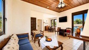 A spacious living area with a wooden ceiling, a dining table with chairs, a sofa, and a TV mounted on the wall. - Ekklisies Tria Large Private Pool, A/C, WiFi (Apokoronos)
