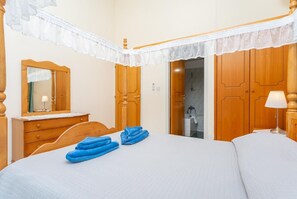 Een slaapkamer met een bed, een houten dressoir, een spiegel en een deur naar de badkamer.