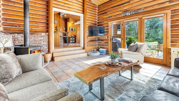 Ein Blockhaus-Interieur mit Kamin, einem an der Wand montierten Fernseher und einer gemütlichen Sitzecke mit Tisch.