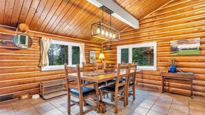 Ein Holzblockhaus-Interieur mit Esstisch, Stühlen, einer Pendelleuchte und einem Bild an der Wand.