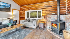 Ein gemütliches Blockhaus-Interieur mit Kamin, Holzwänden, einer Couch und einem Essbereich.