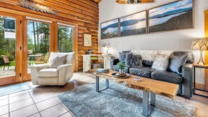 Ein gemütliches Wohnzimmer mit Holzbalkendecke, einer Couch, einem Couchtisch und Blick ins Freie durch große Schiebeglasfenster.