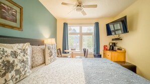 A bedroom with a bed, a desk, a chair, a television, and a window with curtains.