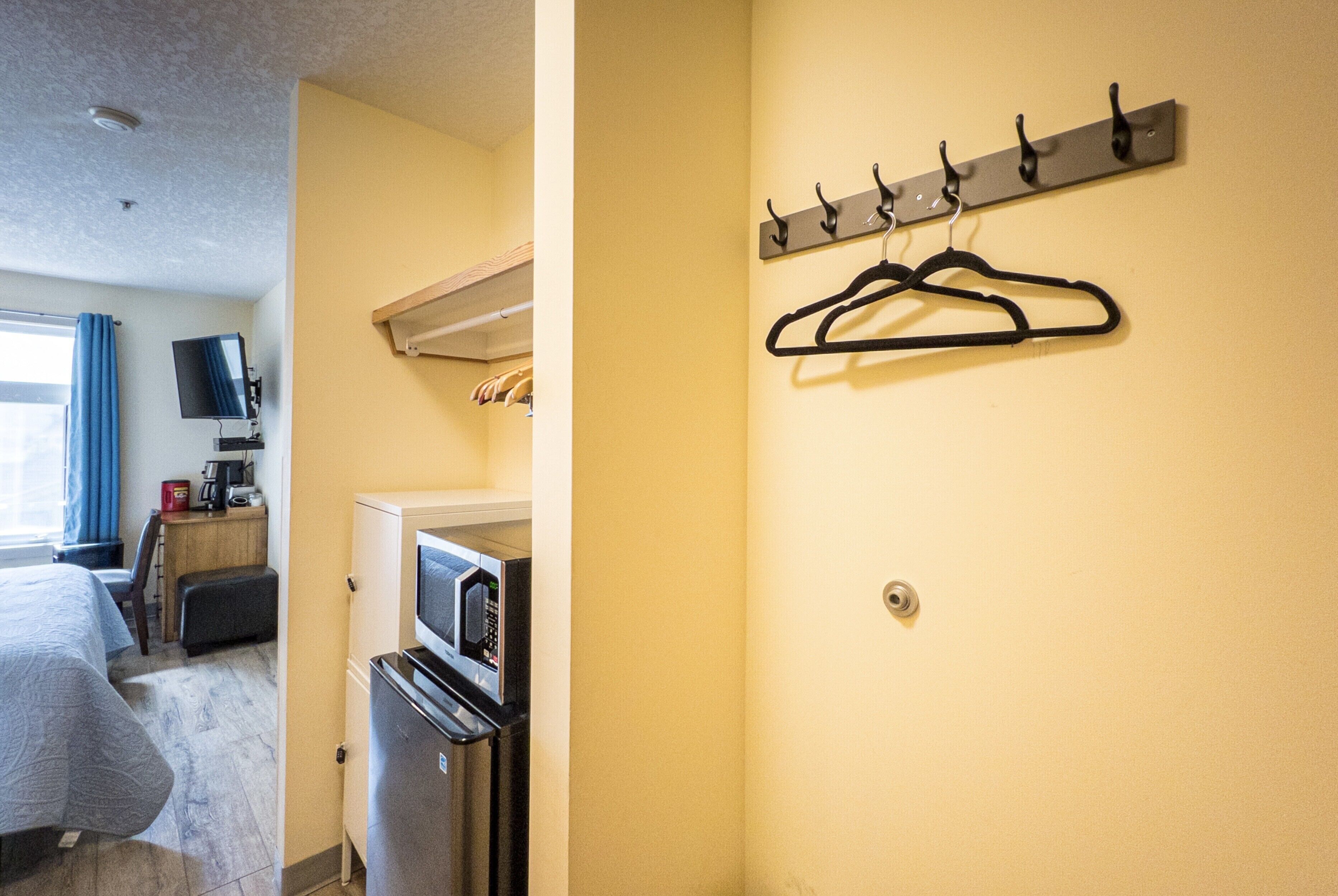 Une chambre d’hôtel équipée d’un lit, d’un bureau avec un ordinateur, d’un four à micro-ondes et d’un porte-manteau avec des cintres.