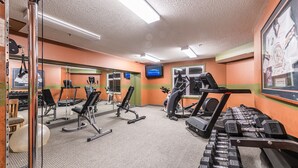 A gym with cardio machines, weight benches, and a television screen.
