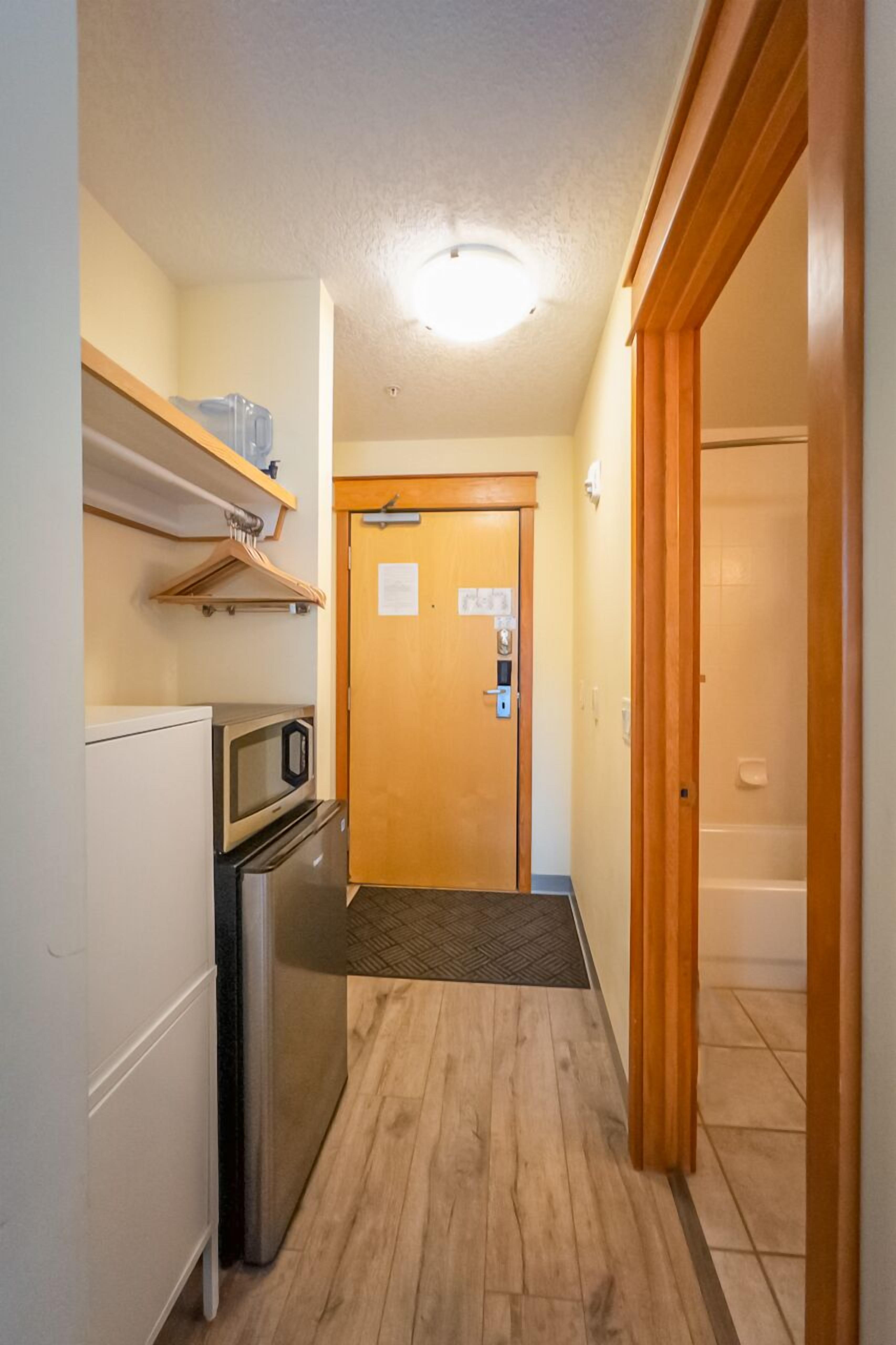 A narrow hallway with a microwave, refrigerator, and wooden door at the end.