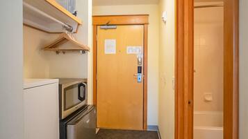 A narrow hallway with a microwave, refrigerator, and wooden door at the end.