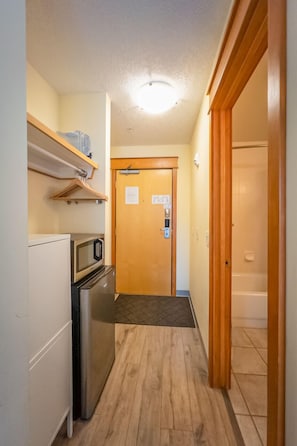 Un couloir étroit, avec un four à micro-ondes, un réfrigérateur et une porte en bois au fond.