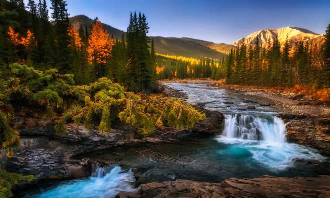 Ein Fluss fließt durch einen Wald mit einem Wasserfall, umgeben von Bergen.