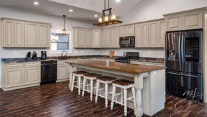 A spacious kitchen with a large island, white cabinetry, stainless steel appliances, and a hanging light fixture. - Norfork Lake: Family Retreat  (Calico Rock)