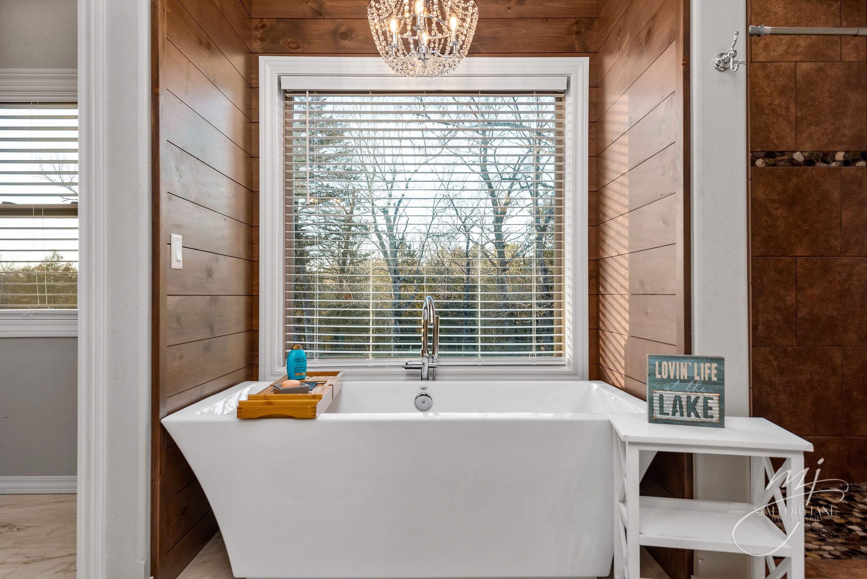 Un bagno con una vasca freestanding, una finestra con persiane, un lampadario e un cartello con scritto "Lovin' Life at the Lake".