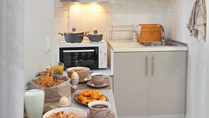 Cocina compacta con microondas, tostadora y un lavamanos pequeño. Hay varios productos para el desayuno en la encimera, como huevos, pan y pasteles.