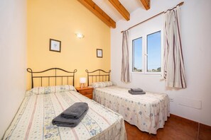 A bedroom with two beds, a window with curtains, a nightstand, and a wall-mounted light. - Villa La Luna - Two Bedroom Villa, Sleeps 4 (Ciutadella de Menorca)