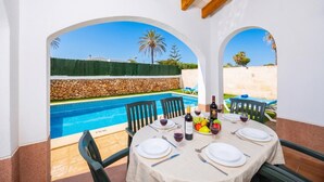 A dining area with a view of a swimming pool, outdoor seating, and a stone wall. - Villa La Luna - Three Bedroom Villa, Sleeps 6 (Ciutadella de Menorca)