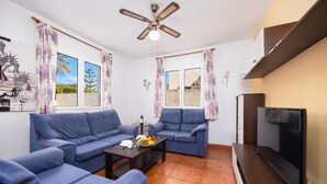 A living room with a sofa set, a coffee table with fruit, a TV, and a ceiling fan. - Villa La Luna - Three Bedroom Villa, Sleeps 6 (Ciutadella de Menorca)