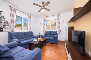 A living room with a sofa set, a coffee table with fruit, a TV, and a ceiling fan. - Villa La Luna - Three Bedroom Villa, Sleeps 6 (Ciutadella de Menorca)