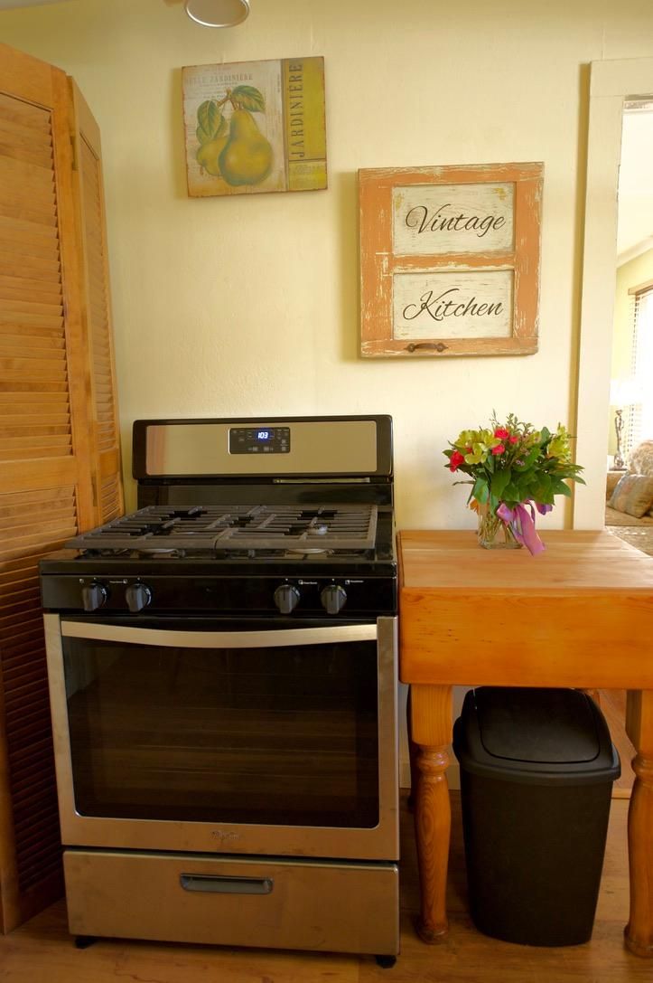 A kitchen with a gas stove, oven, wooden table, and a trash bin.