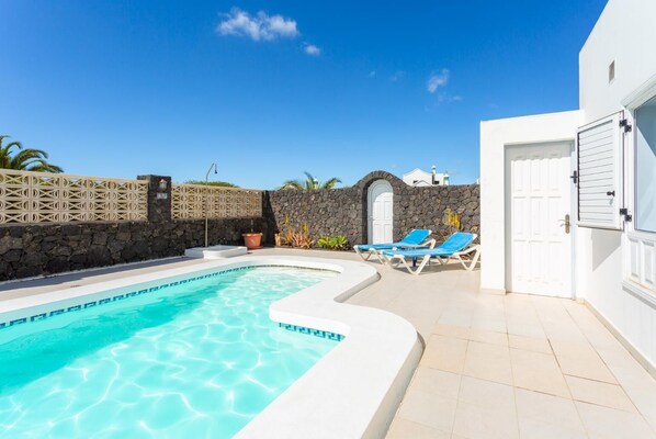 Una piscina con bordo curvo, un muro in pietra e una porta bianca con una finestra.
